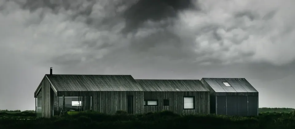 A low timber clad house beside a river, dusk